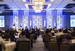 A ballroom set for an investor summit with a speaker on stage